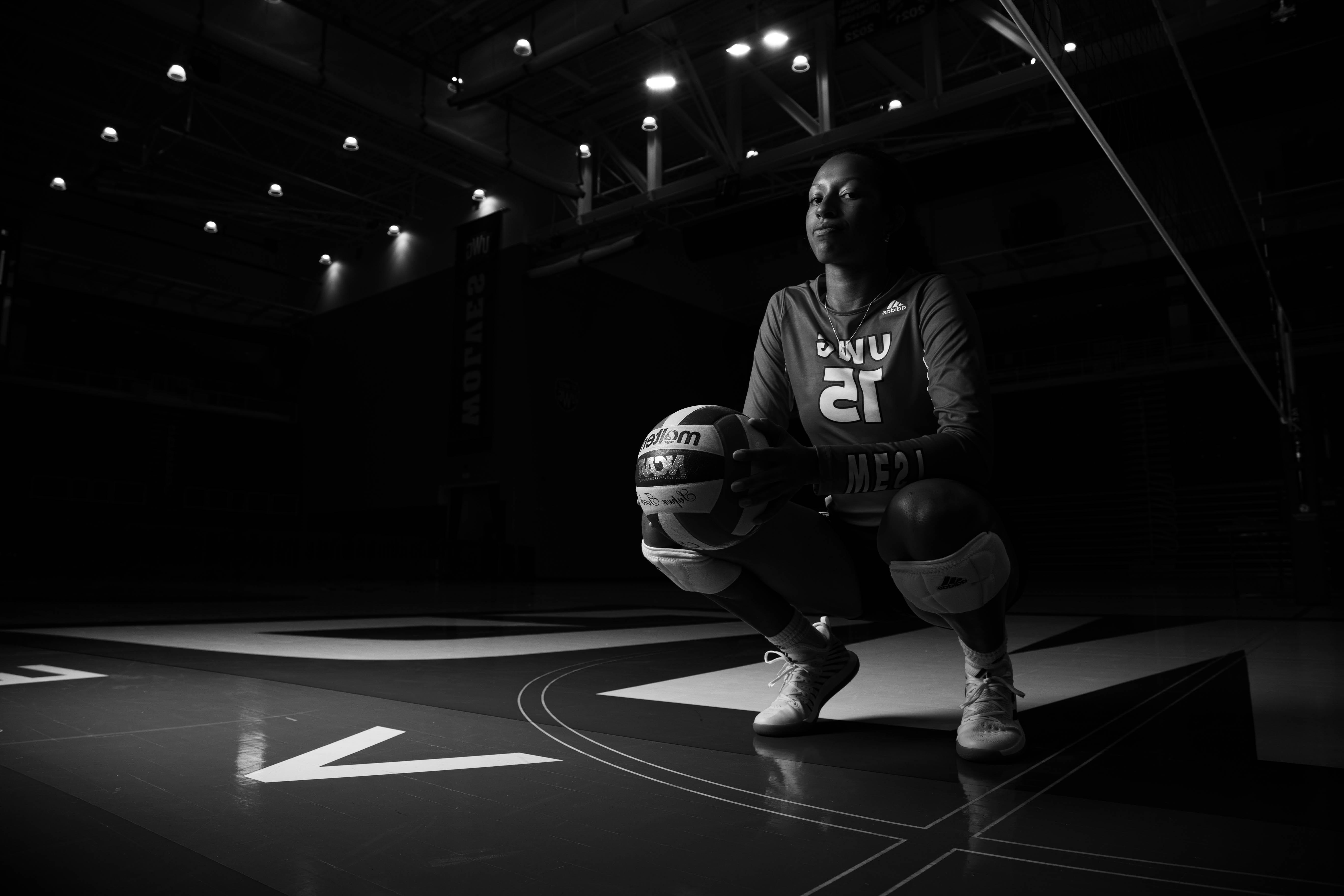 Volleyball player squatting on the court holding a volleyball.